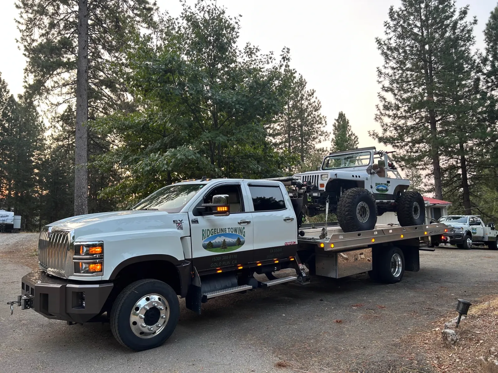 Ridgeline Towing flatbed loaded with a lifted Jeep rock crawler under Sierra pines