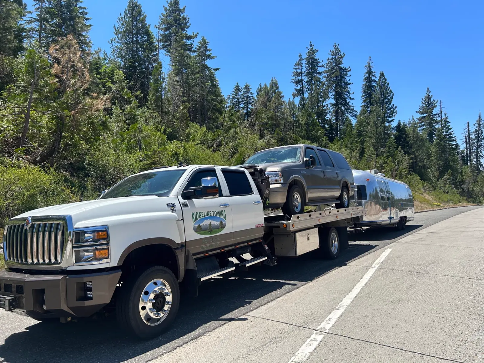 Ridgeline Towing flatbed carrying an SUV and towing an Airstream trailer on a mountain highway