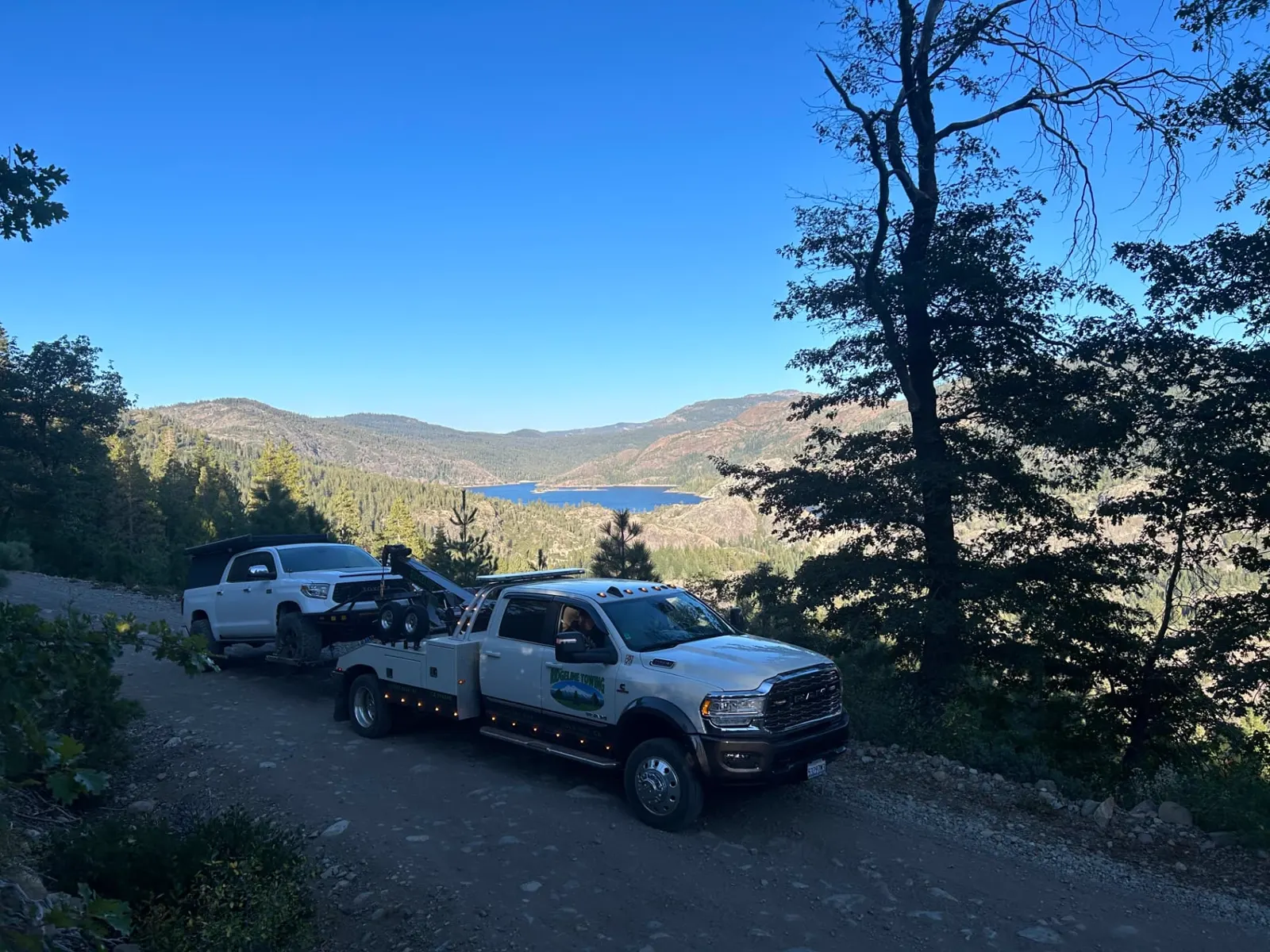Ridgeline Towing wrecker towing a pickup on a forest road above a Sierra Nevada reservoir